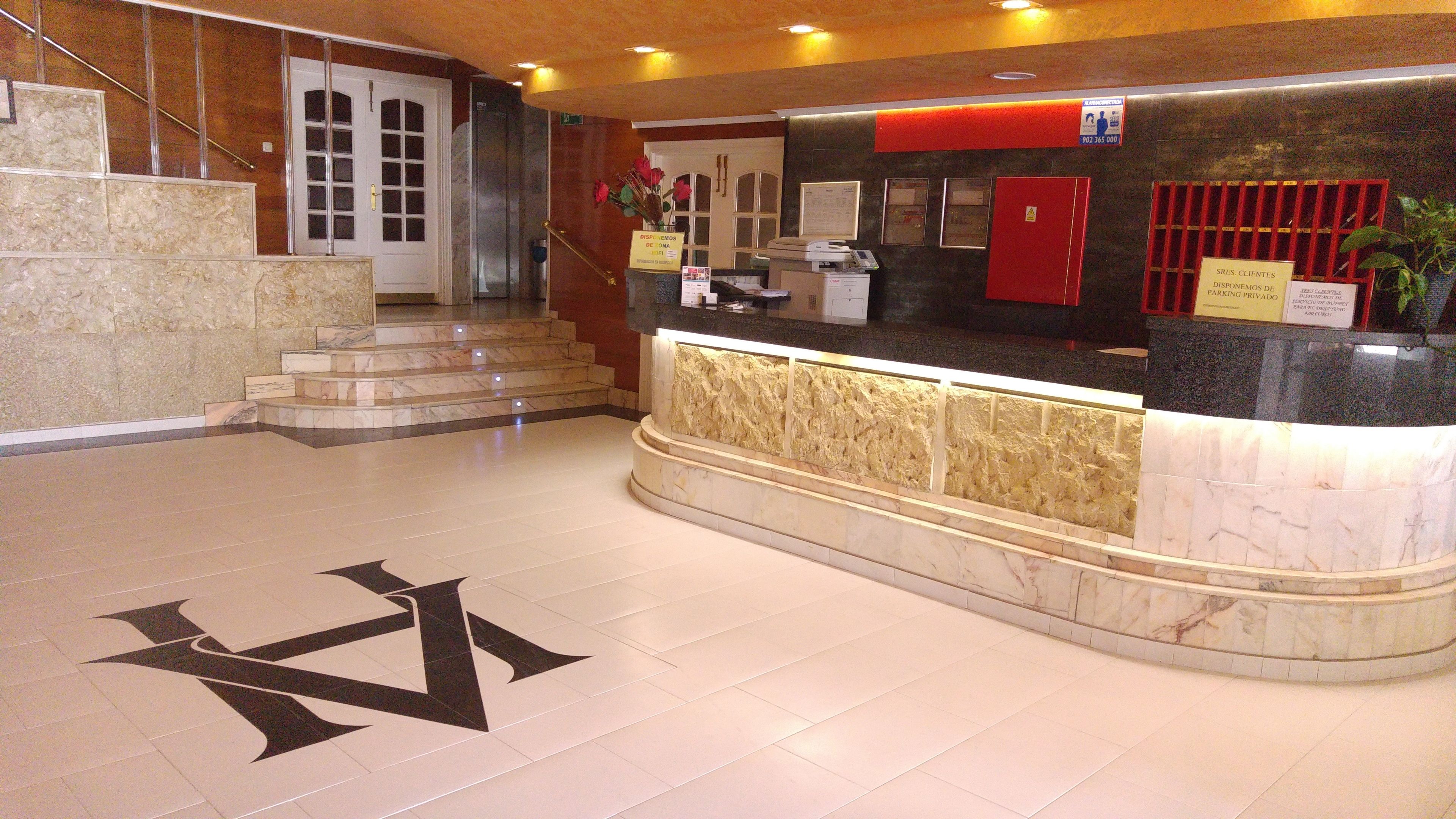 Zona de recepción de hotel con mostrador de mármol, una escalera y un gran símbolo de estrella en el suelo.