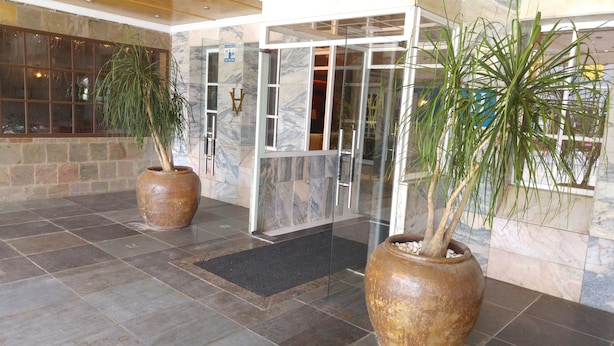 Un'hall con pavimento in marmo, porte in vetro e due grandi piante in vaso.