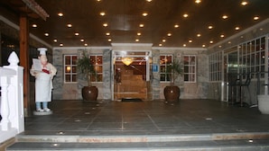 Ingresso di un hotel con pavimento in marmo, reception e due grandi piante in vaso.