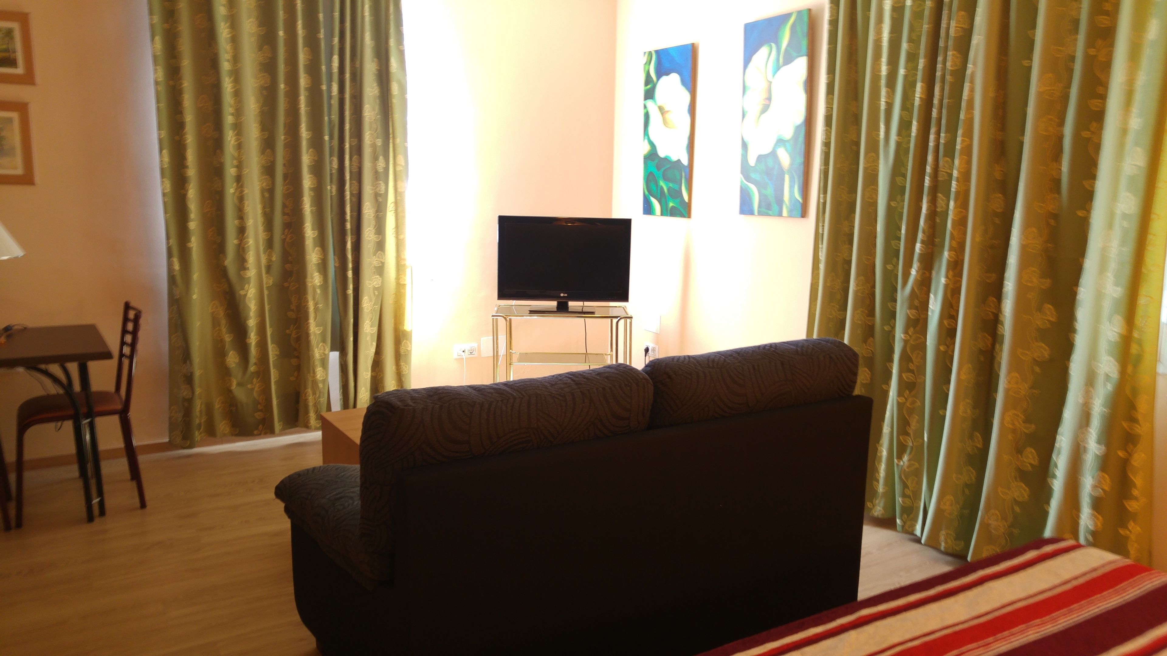 Una habitación de hotel con un sofá, un televisor en un mueble bajo, una mesa y una silla.
