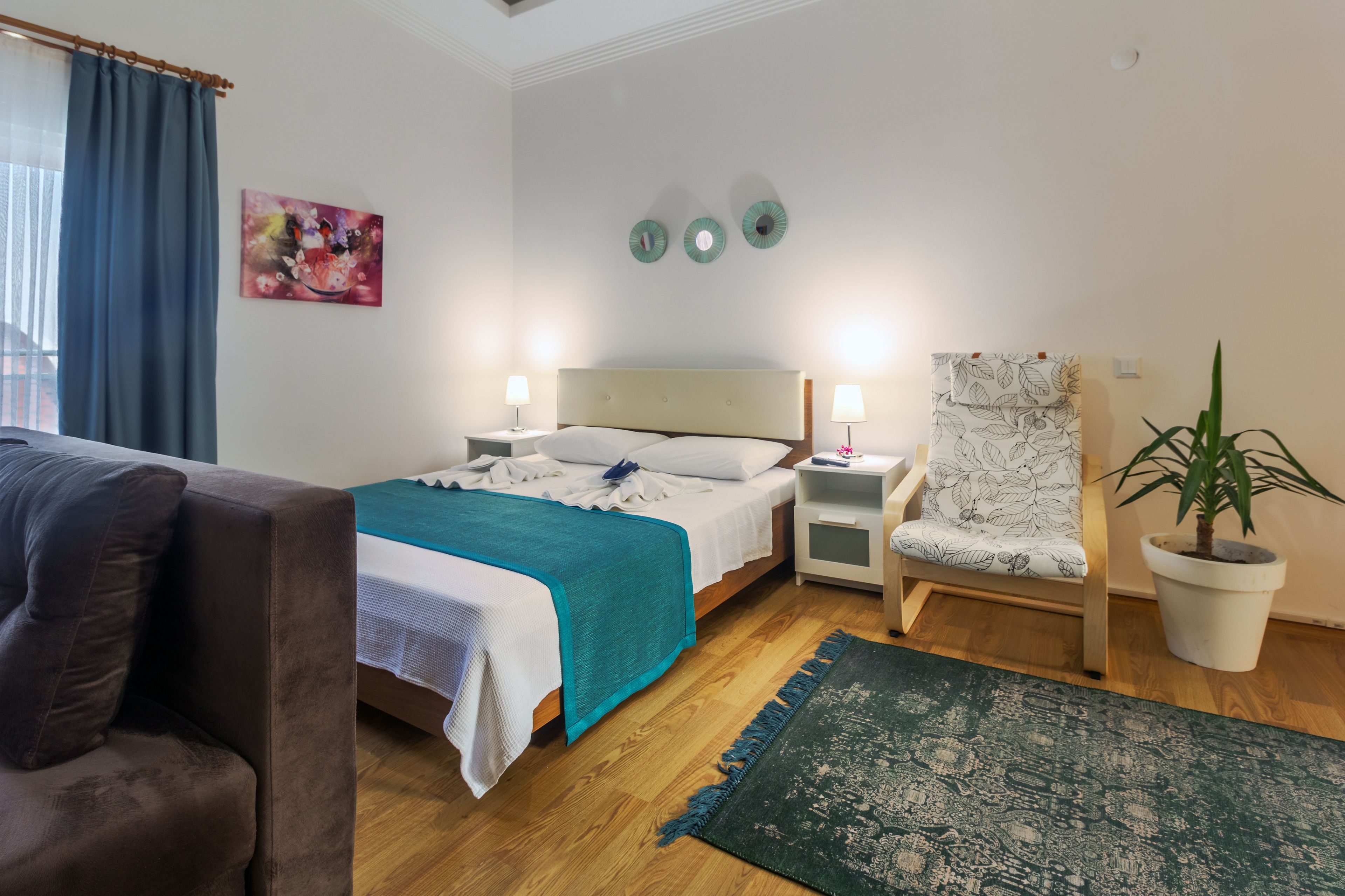 Een hotelkamer met een bed, een stoel, een kamerplant en een schilderij aan de muur.