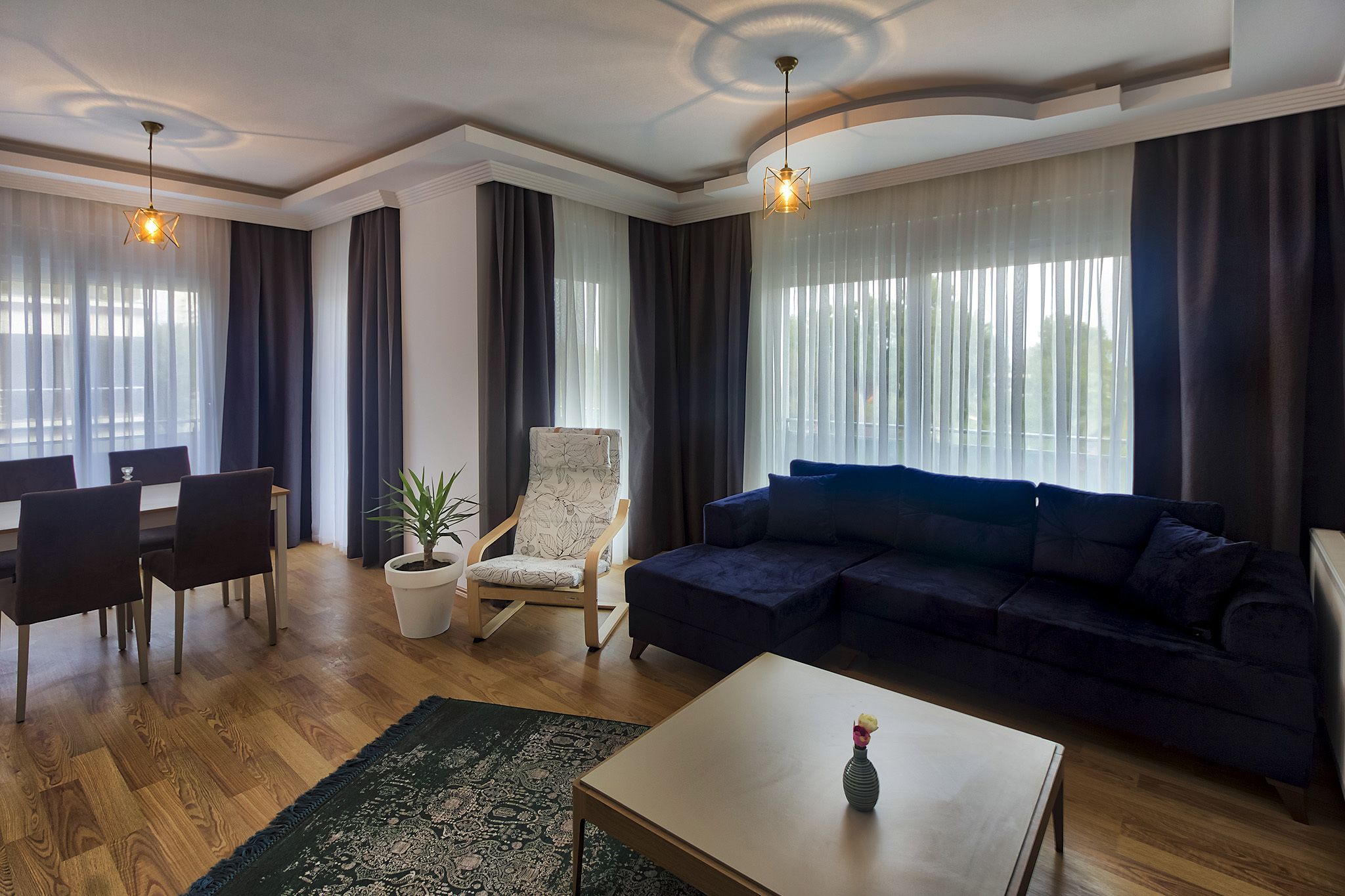 A modern living room with a dark blue sofa, a wooden coffee table, a dining area with a table and chairs, and a potted plant.