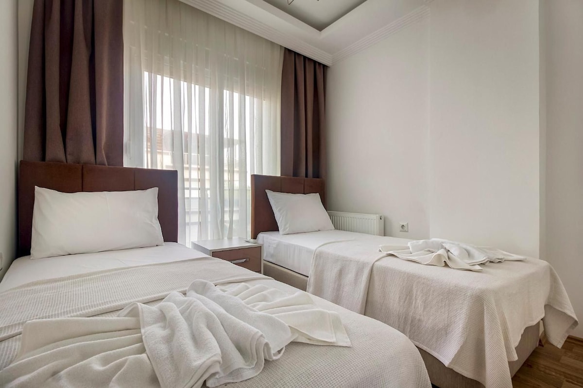 A hotel room with two beds, a nightstand, and a window with curtains.