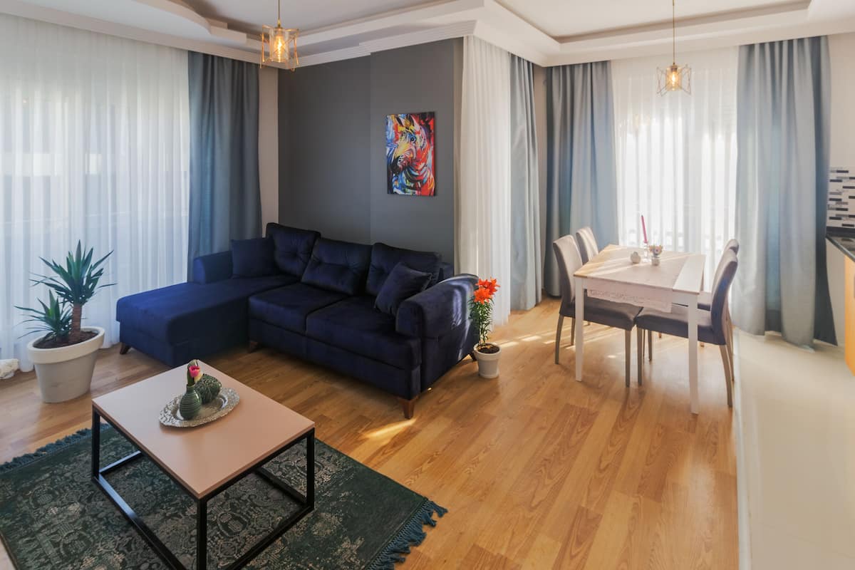 A modern living room with a dark blue sectional sofa, a wooden coffee table, and a dining area with a white table and chairs.