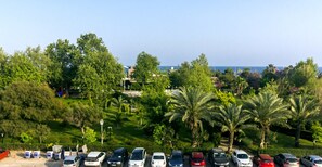 A parking lot with various cars and lush greenery, including palm trees, in a sunny outdoor setting. - Aspendos Seaside (Konyaalti)