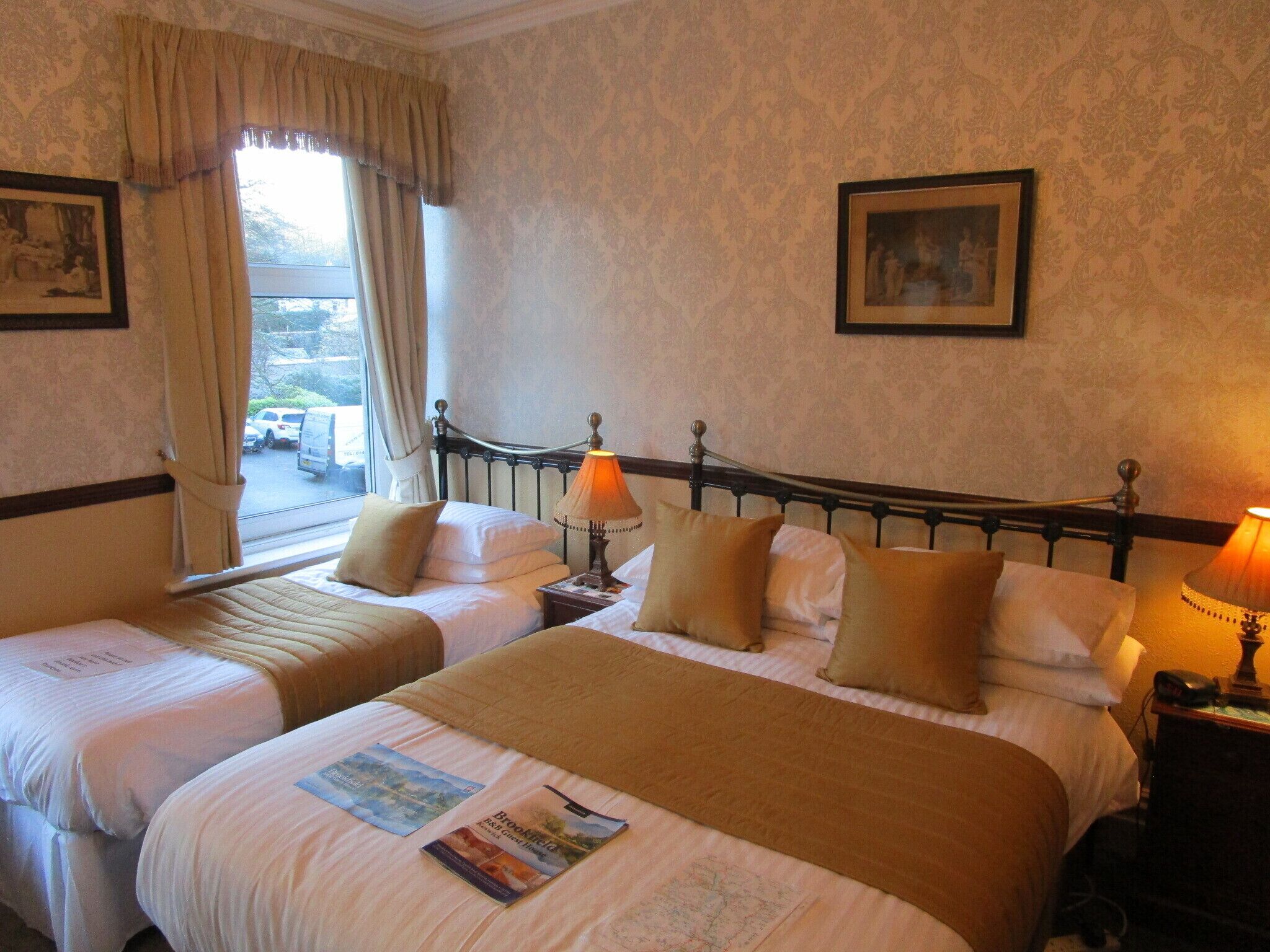 A hotel room with two beds, a window with curtains, a lamp on each side, and a framed picture on the wall.