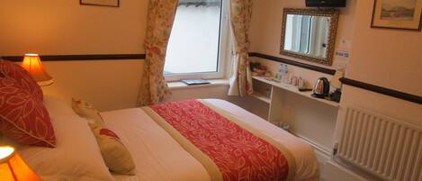 Hotelkamer met een bed, nachtlampjes, een raam met gordijnen, een spiegel, een televisie en een radiator.