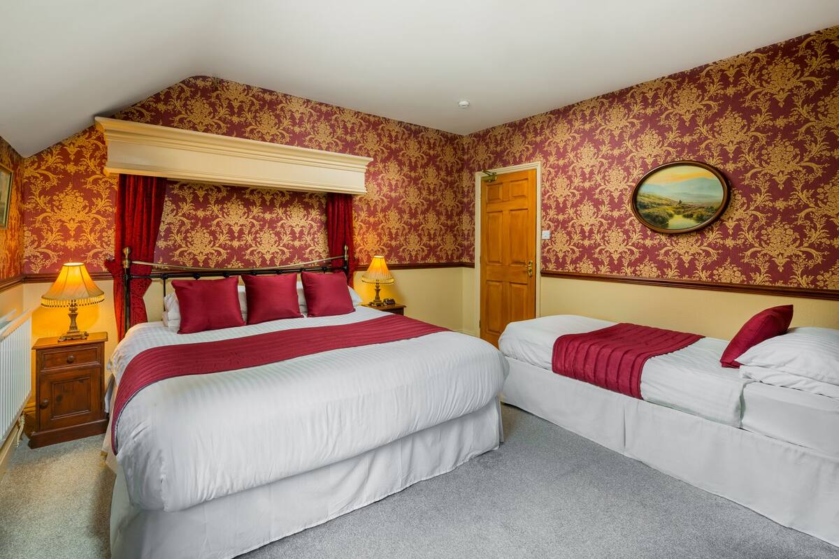 A bedroom with two beds, a wooden headboard, red curtains, a painting, and a wooden door.