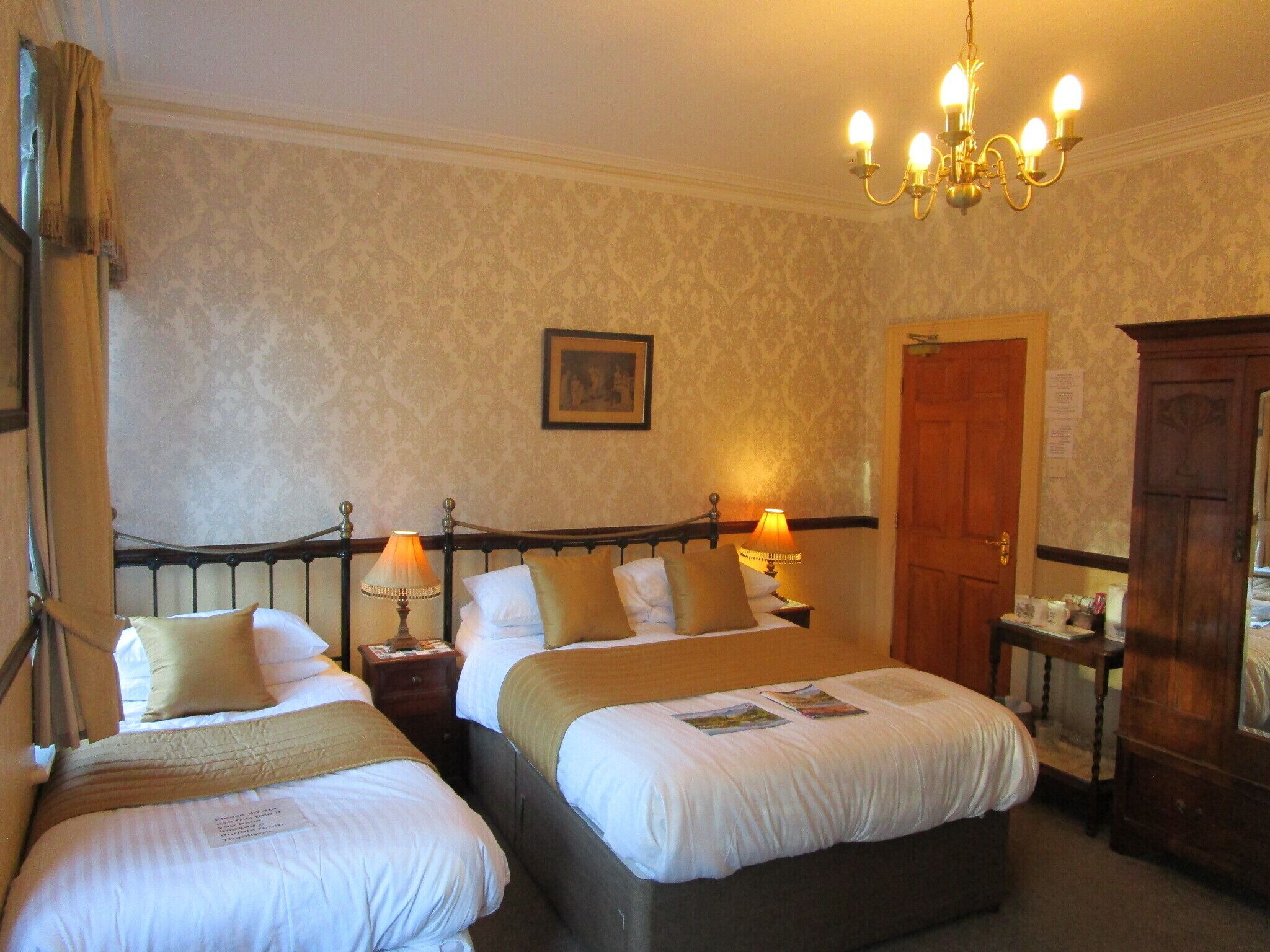 Une chambre d’hôtel avec deux lits, un lustre, une armoire en bois et une porte.