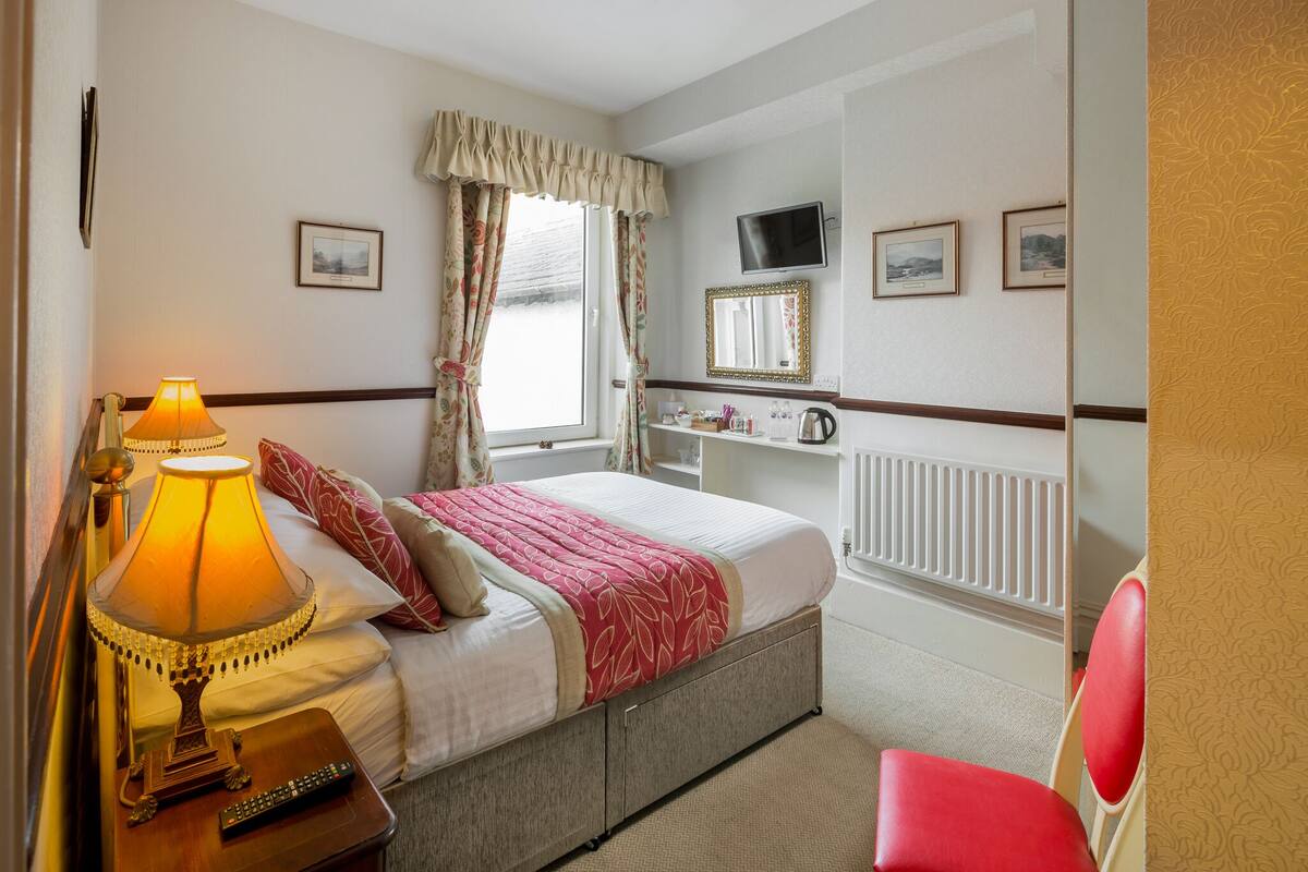 A bedroom with a bed, bedside lamp, TV, and a chair.