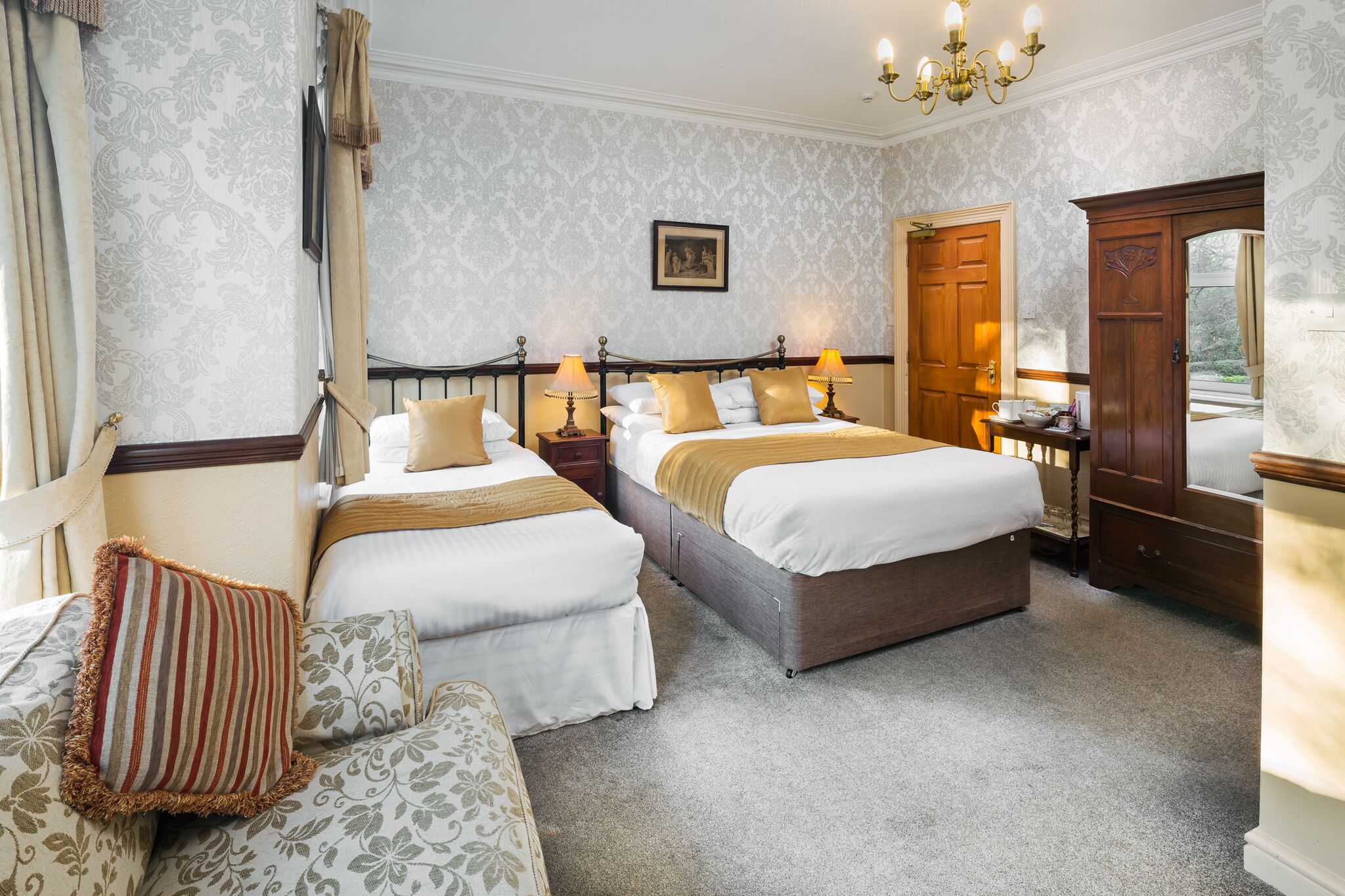 A hotel room with two beds, a sitting area, and a wardrobe.
