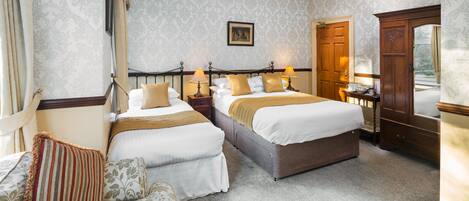 A hotel room with two beds, a sitting area, and a wardrobe.