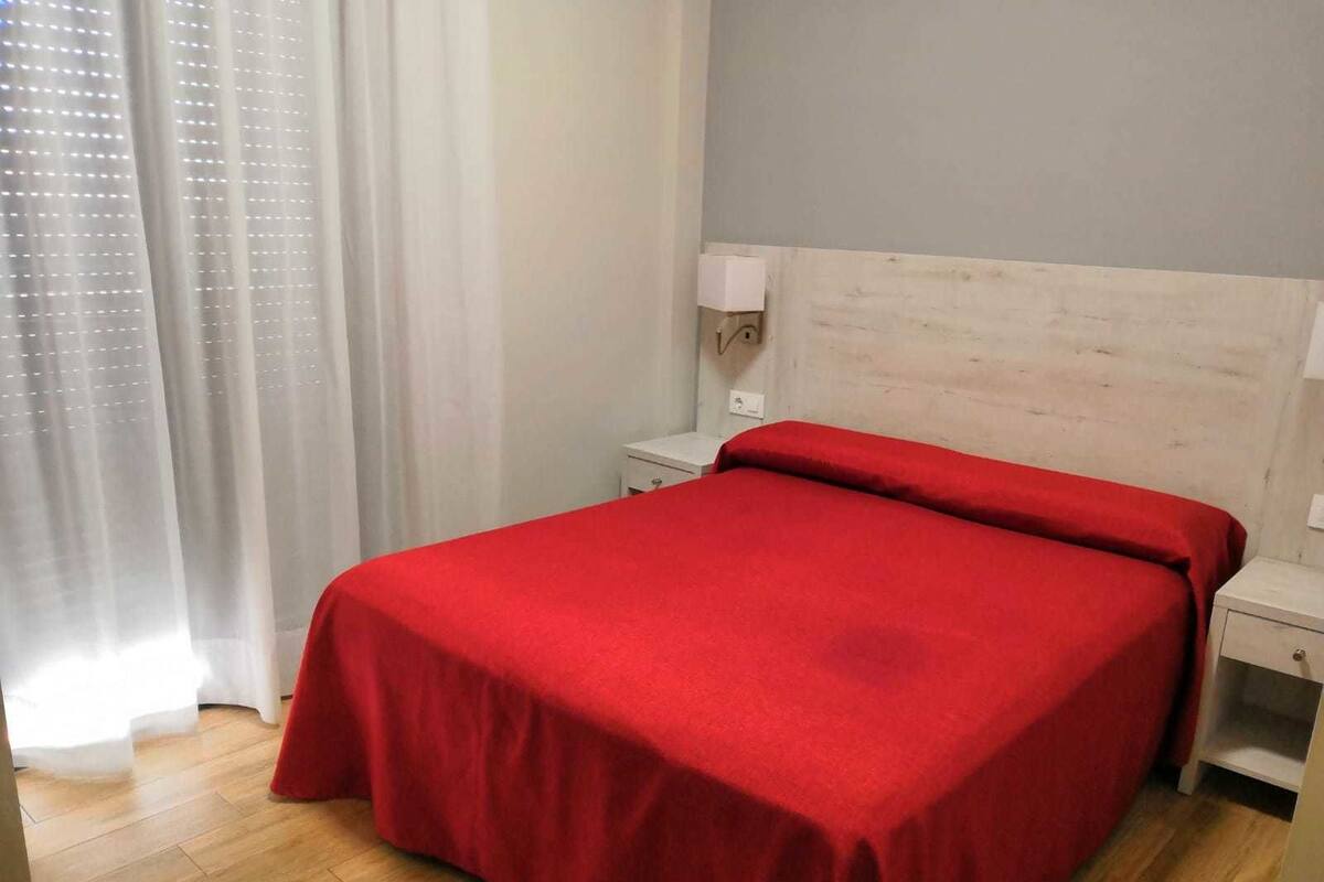Una habitación con una cama, una mesita de noche, una lámpara y una ventana con cortinas.