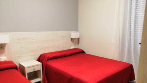 Habitación con dos camas individuales, cada una con una colcha roja, una mesita de noche y una lámpara de pared.