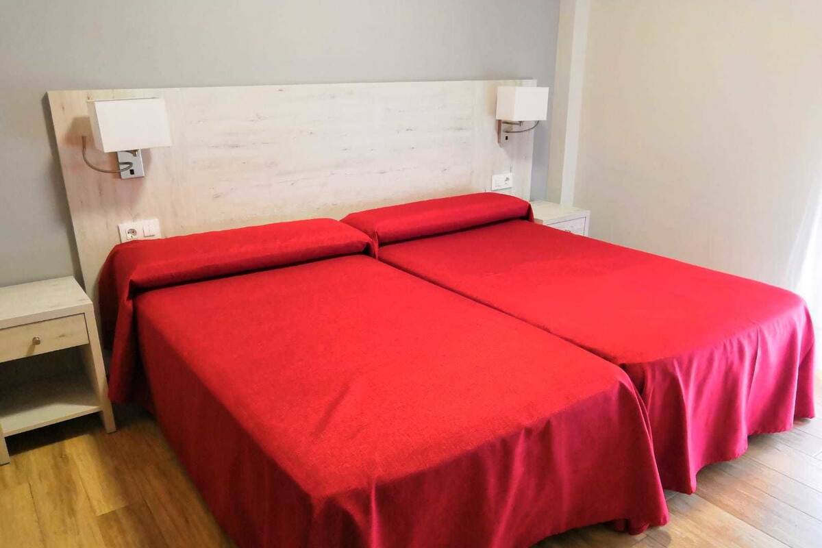 Una cama doble con ropa de cama roja, cabecera de madera, lámparas de noche y mesita de noche.