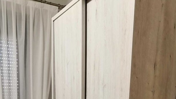 Una habitación con un armario, una pequeña estantería y una cortina.