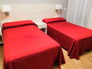 Una habitación con dos camas individuales, cada una con colcha roja, cabecero de madera y lámparas de noche.