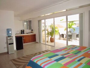 A hotel room with a bed, a kitchenette, a water dispenser, and a sliding glass door leading to an outdoor patio with a table and chairs. - Arcoiris Dreams by Playa Paradise (Playa del Carmen)