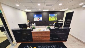 Un área de recepción con dos mostradores de mármol negro, una mesa de recepción y dos pantallas grandes que muestran imágenes. Un suelo de moqueta negra con los logotipos de Lava Grill y Boardwalk.