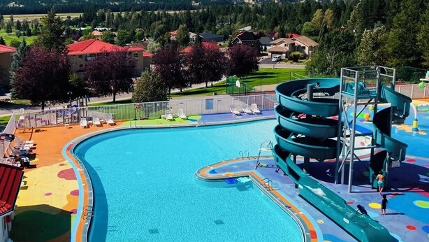 Una piscina con un deck colorido, un tobogán de agua y vistas a montañas al fondo.
