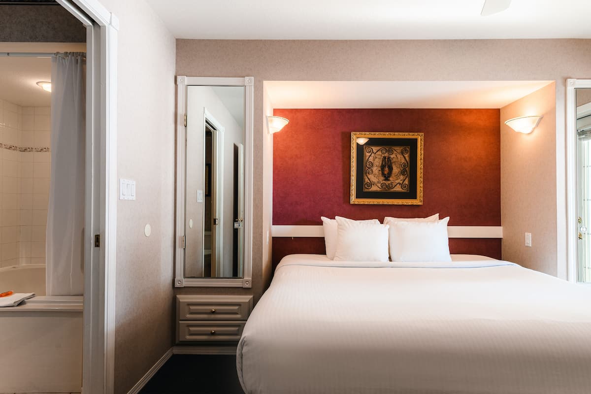 Habitación de hotel con una cama grande, un espejo, una obra de arte enmarcada en la pared y un baño visible a través de una puerta abierta.