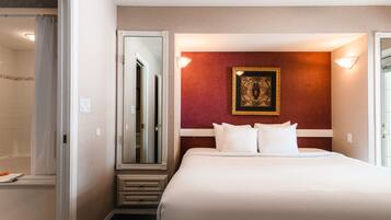 A hotel room with a large bed, a mirror, a framed artwork on the wall, and a bathroom visible through an open door.