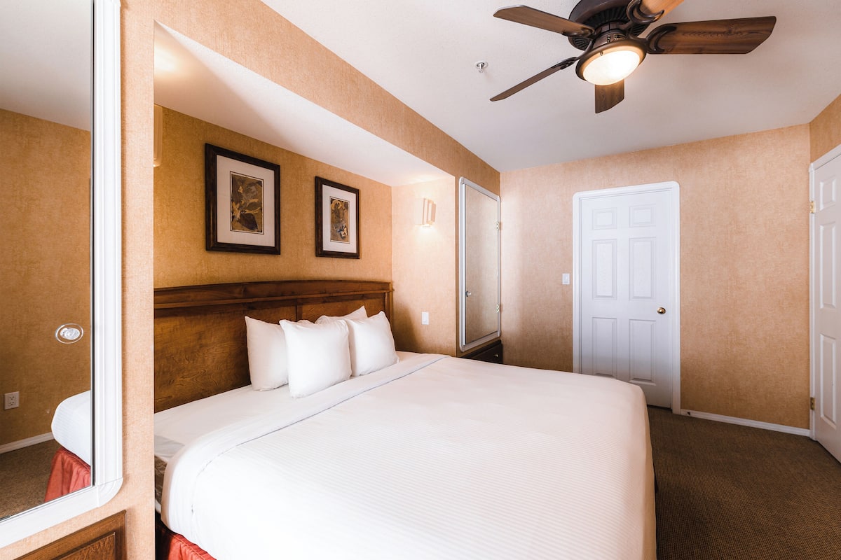Una habitación de hotel con una cama grande, un ventilador de techo y dos cuadros en la pared.