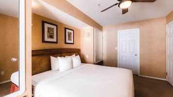 Quarto de hotel com uma cama grande, um ventilador de teto e duas fotos emolduradas na parede.