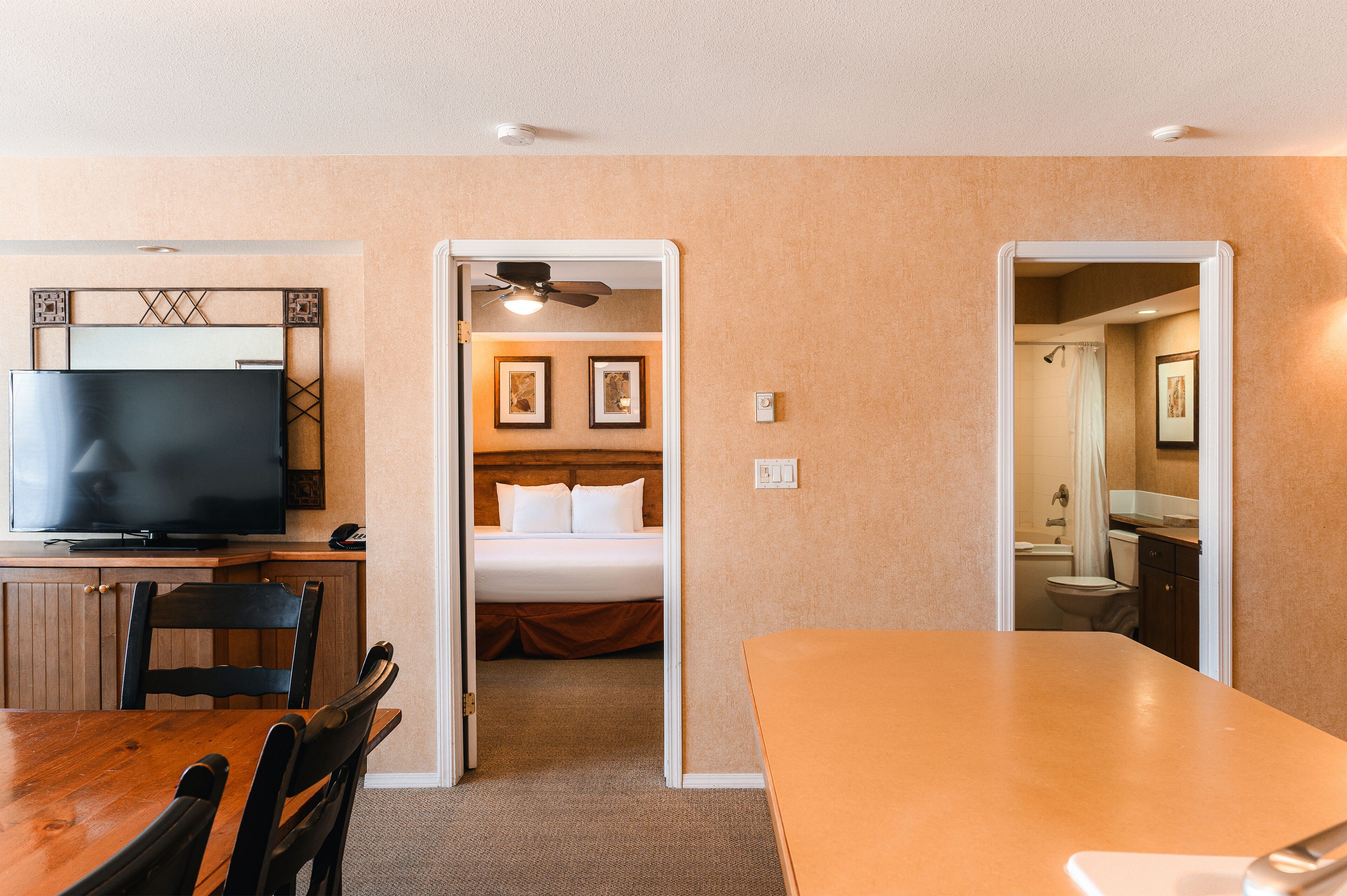 A hotel room with a TV, dining table, chairs, a bed, and a bathroom visible through an open door.