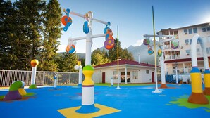 Zona de juegos al aire libre con equipo colorido y un edificio al fondo.