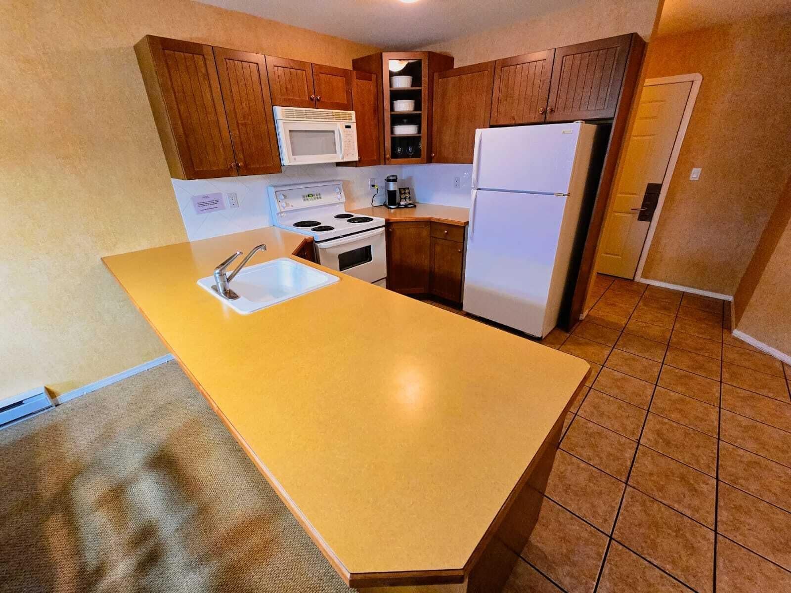 A kitchen with wooden cabinets, a white stove, a microwave, a refrigerator, and a sink.