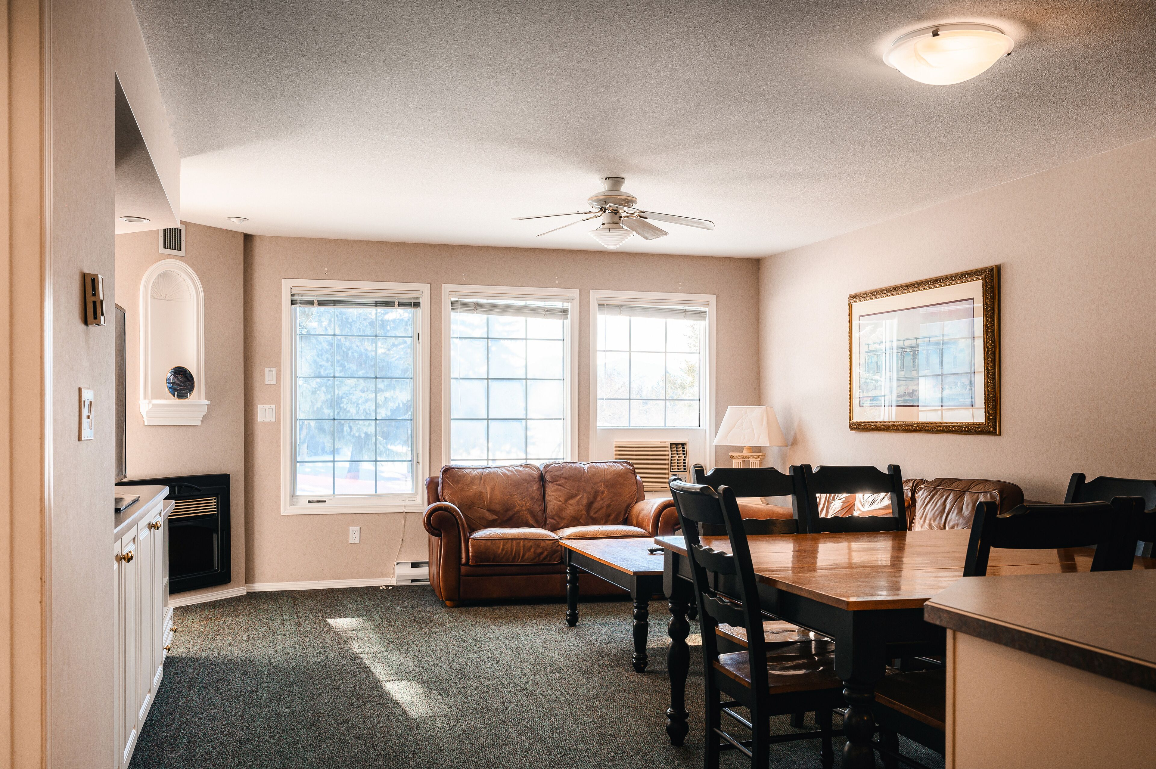 A dining area with a table and chairs, a brown leather sofa, and a ceiling fan.