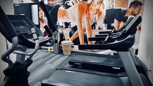 Un gimnasio con cintas de correr, un cesto y una botella de agua en el suelo.