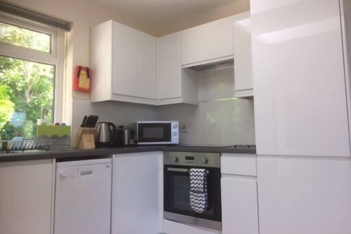 A compact kitchen with white cabinets, a microwave, an oven, and a window with a view of greenery.
