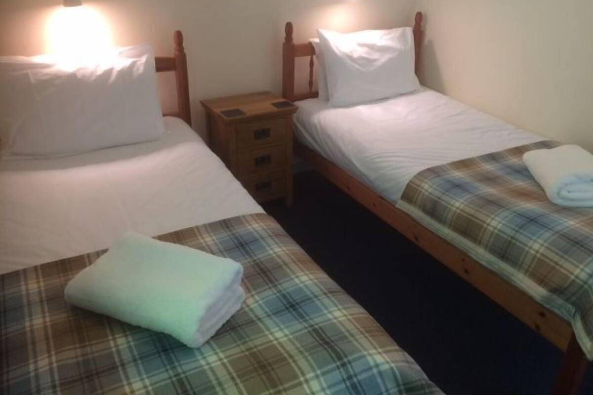 A room with two single beds, each with a wooden headboard, white bedding, and a small wooden nightstand with drawers.