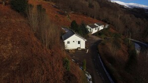 Uma casa de campo com telhado inclinado, um pequeno alpendre e um caminho que a leva até ela.