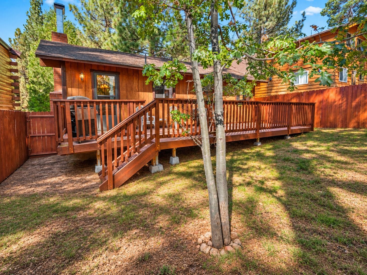A wooden cabin with a deck, a staircase, and a small tree in the yard.