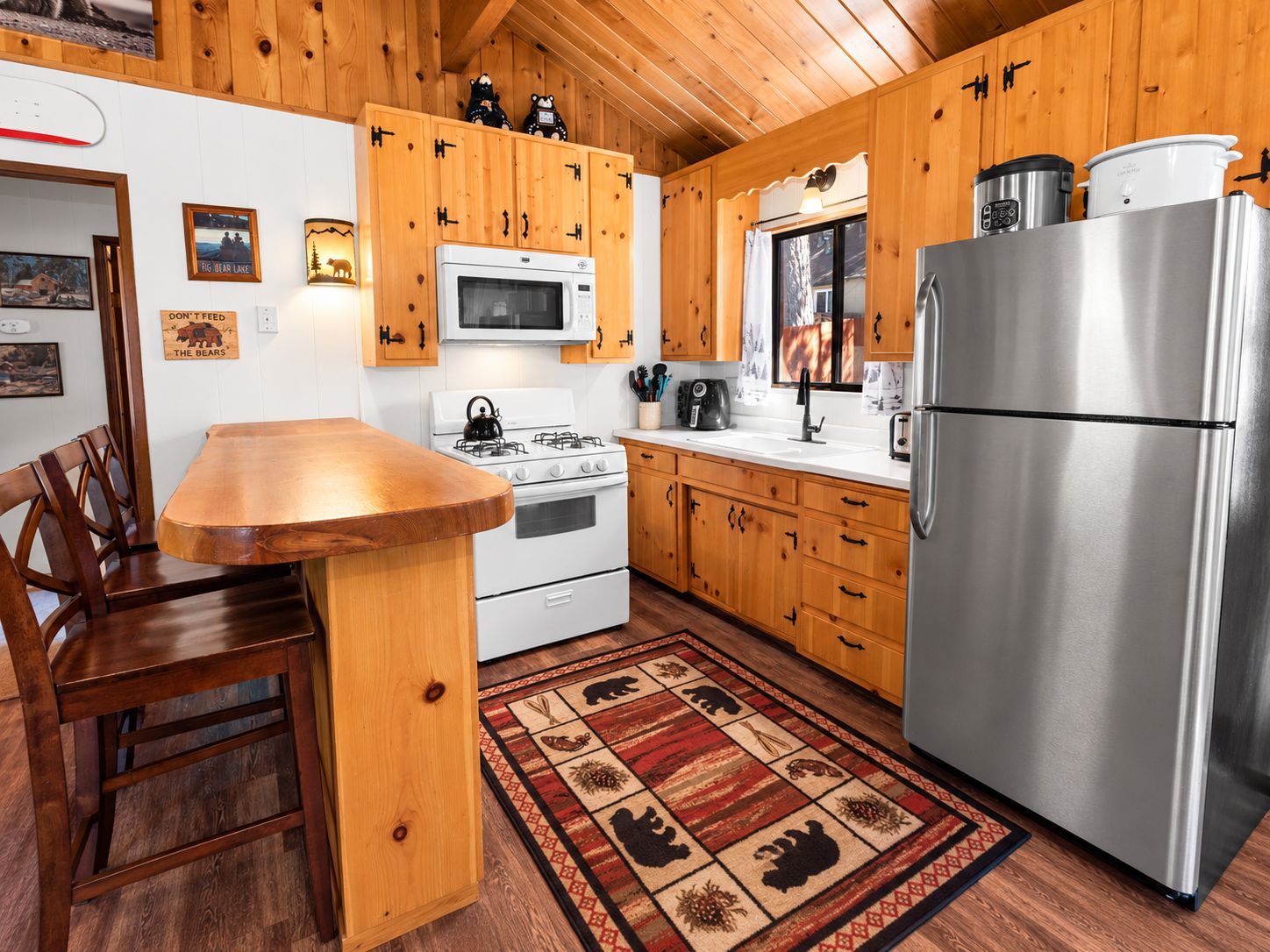 Une cuisine avec des meubles de rangement en bois, un réfrigérateur en acier inoxydable, un four à micro-ondes, une cuisinière et une table à manger en bois, accompagnée de chaises.