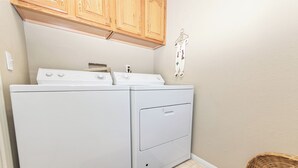 A laundry room with two white washers and dryers, wooden cabinets above, a gray rug, and a wicker basket. - Bear Mountain Escape Condo (Big Bear Lake)