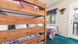 A bunk bed with a quilted bedspread, a window with a view of trees, and a door with a basket on the wall. - Bear Mountain Escape Condo (Big Bear Lake)