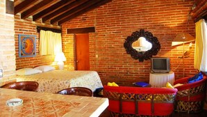 A cozy room with a brick wall, a bed, a television, and a red chair.