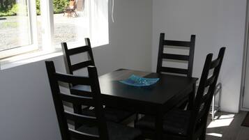 Un coin repas avec une table et quatre chaises, un objet décoratif bleu posé sur la table, et une vue sur l’extérieur par une fenêtre.