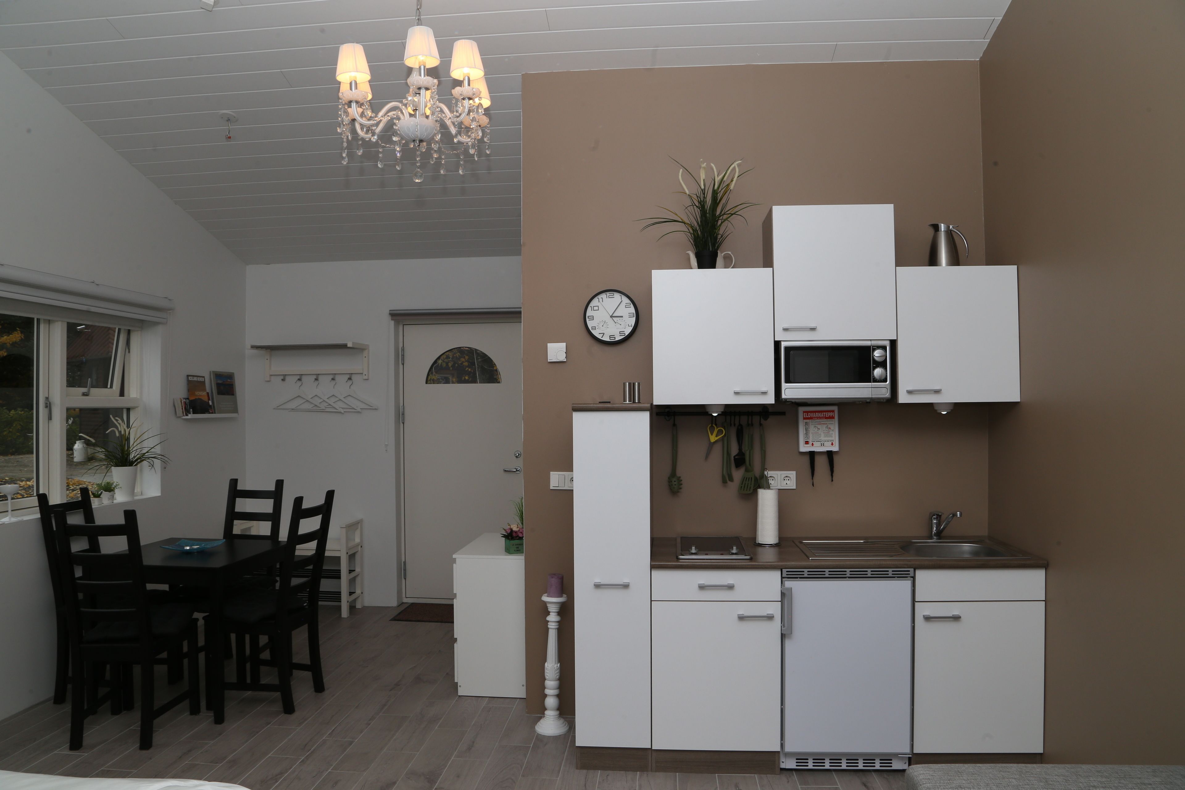 Cozinha compacta com armários brancos, micro-ondas e pia. Possui uma área de refeições com mesa e cadeiras.