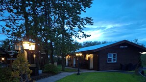 A wooden cabin with a well-maintained lawn, a small tree, and a pathway leading to the entrance. - Country Dream guesthouse (Selfoss)