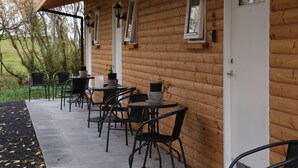A wooden cabin with a covered patio area featuring outdoor seating and tables, surrounded by trees. - Country Dream guesthouse (Selfoss)
