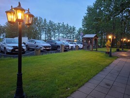 Pysäköintialue, jossa on autoja, valaisinpylväs ja pieni puinen rakennelma.