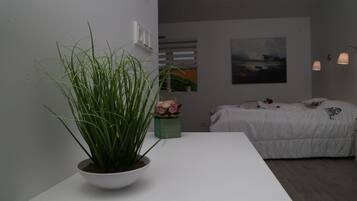 Un dormitorio moderno con una cama blanca, una pequeña planta en maceta y un cuadro en la pared.