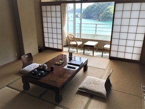 Ein traditioneller japanischer Raum mit Tatami-Böden, einem niedrigen Holztisch und Blick auf eine Küstenlandschaft durch Shoji-Schirme.