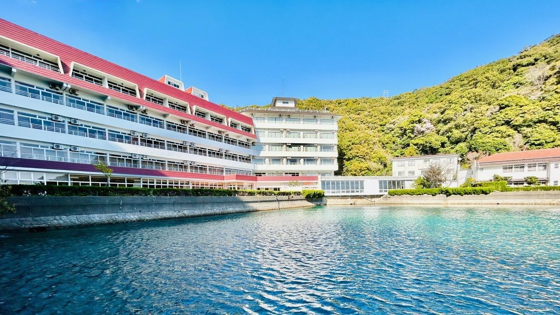 A multi-story hotel with a swimming pool, located near a hillside.