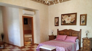 Un dormitorio con suelo a cuadros, cama de madera con ropa de cama rosa, dos mesitas de noche con lámparas y cuadros de flores en la pared.